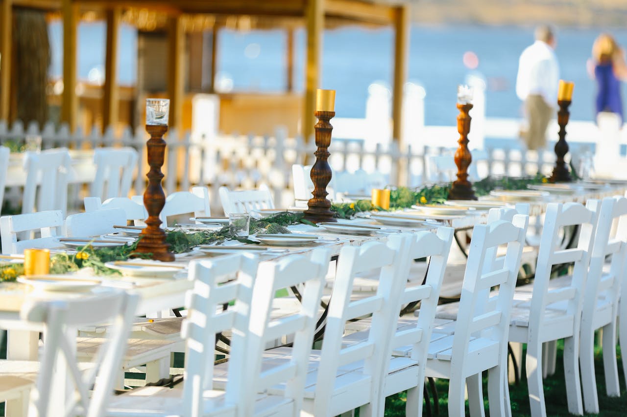 Beautiful outdoor wedding reception with white chairs and decorated tables by the seaside.